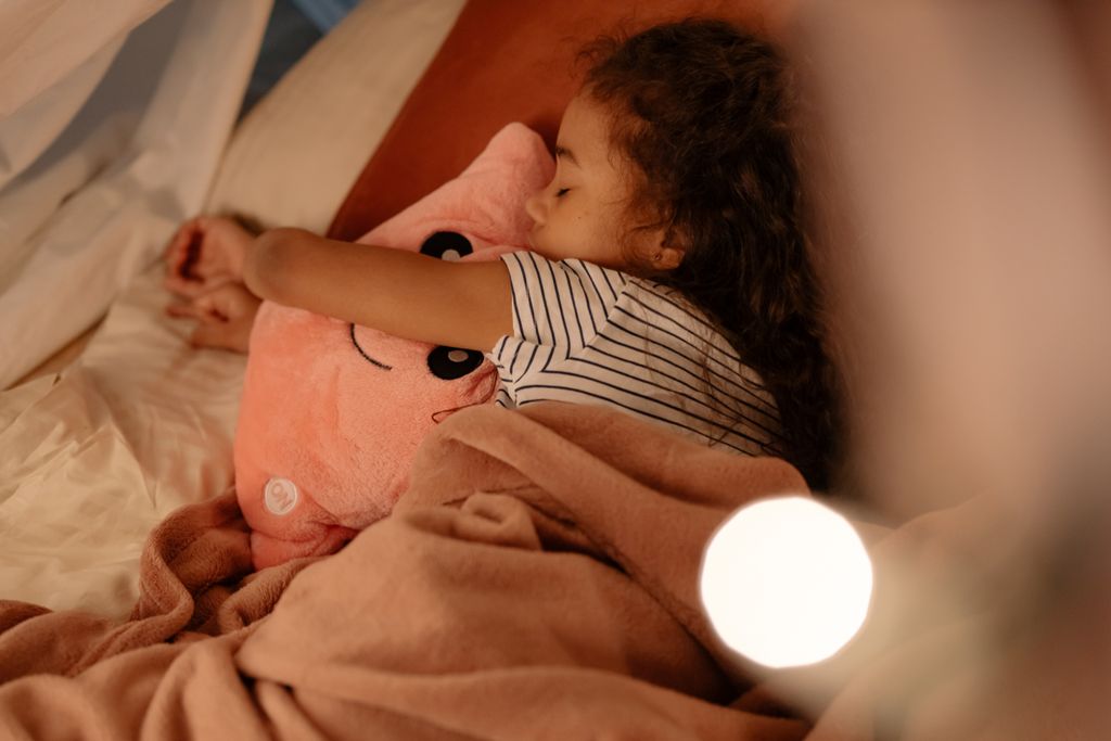 A peaceful scene of a young girl embracing a pink plush toy while sleeping comfortably in her cozy bed.